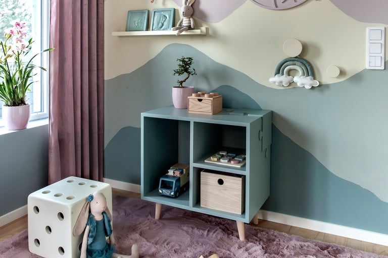 Ett barnrum med en hylla, en tärningspall, leksaker och en väggmålning.