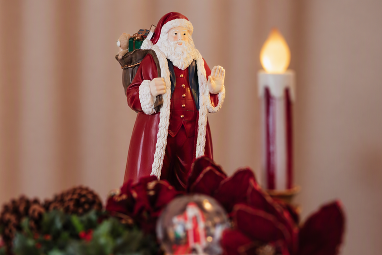 Julgransfigur av tomte med säck med julklappar, placerad i en juldekoration med ljus.
