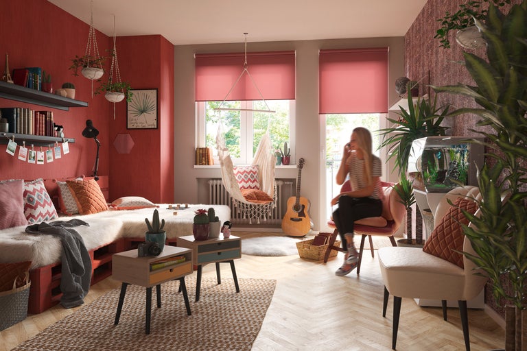 Vardagsrum med säng av lastpallar, hängfåtölj och kvinna i telefon