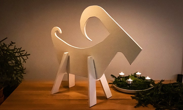 Dekorativ träbock bredvid adventskrans med brinnande ljus på ett bord.