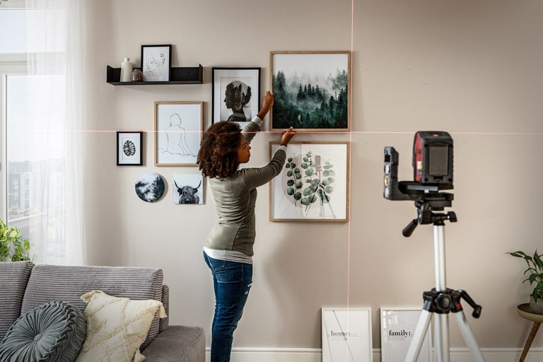 En kvinna hänger upp bilder på en vägg i vardagsrummet med en laseranordning.