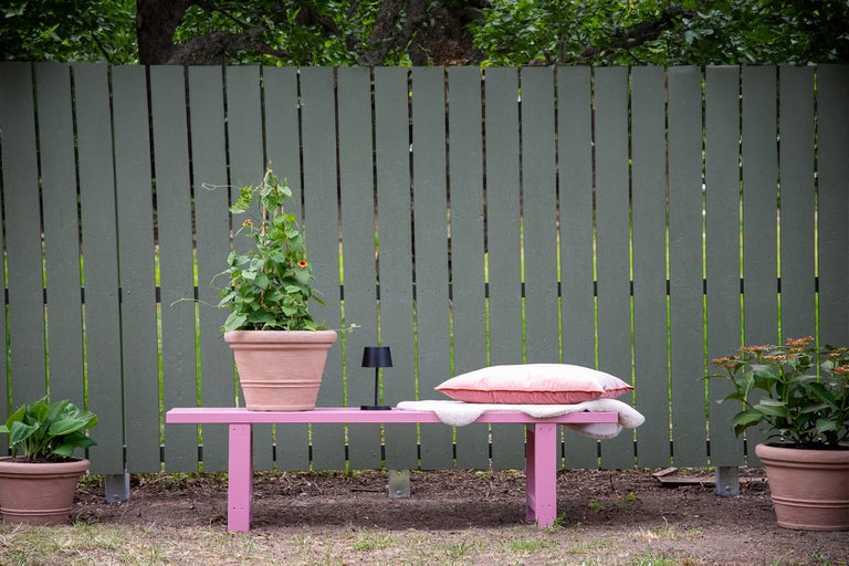 Trädgårdsscen med trästaket, bänk, växter i krukor, kudde och lampa