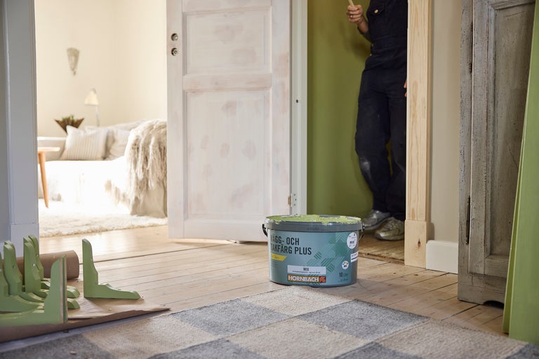 Hink Hornbach Vägg- och Takfärg Plus i ett ljust rum vid renoveringsarbete med en grön vägg och Hornbach Logo.