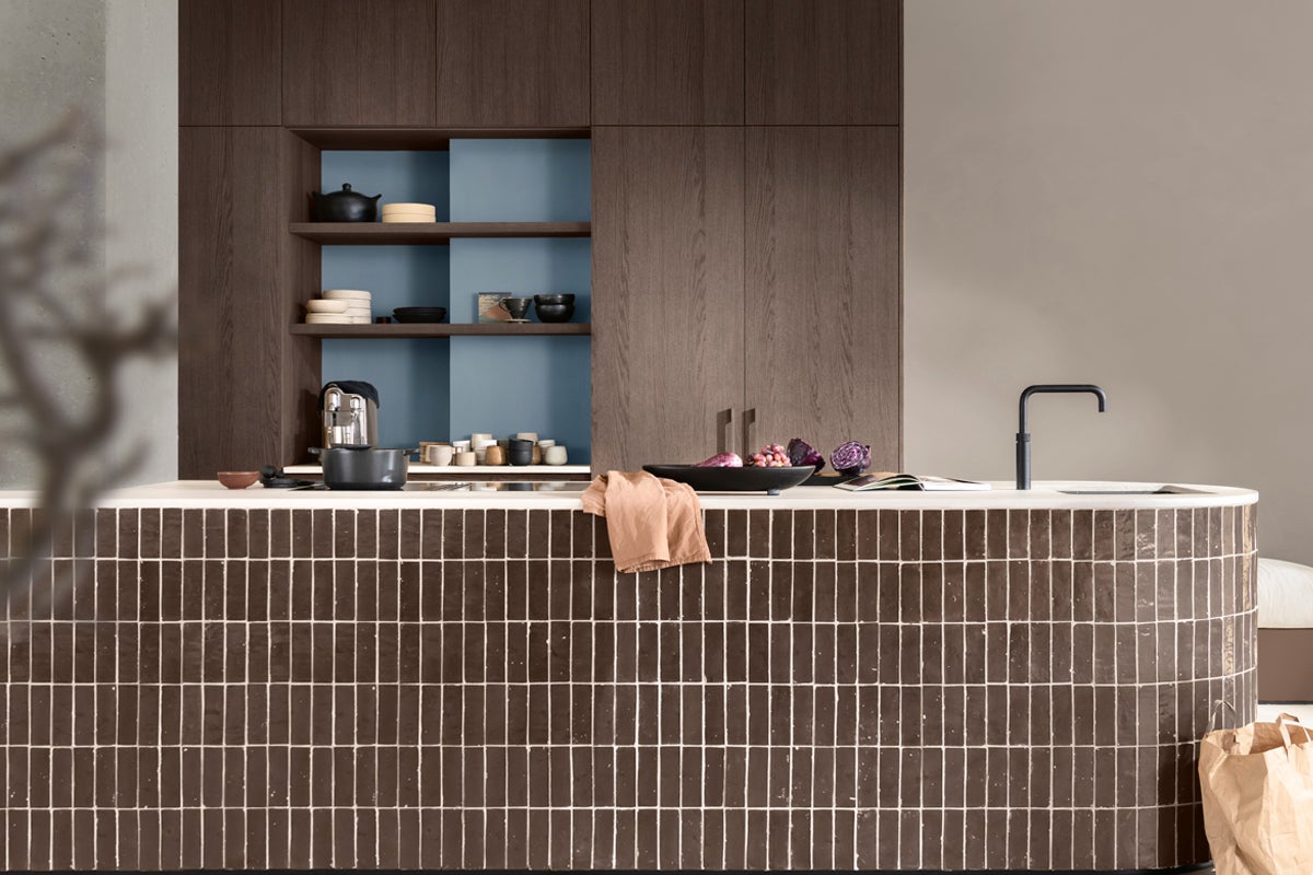 Köksscen med köksö, köksblandare och köksredskap framför en vägg med träskåp med hyllor