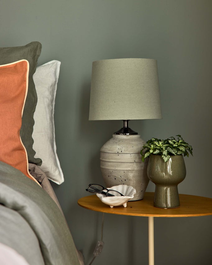 Sängbord med lampa, krukväxt, glasögon och kuddar