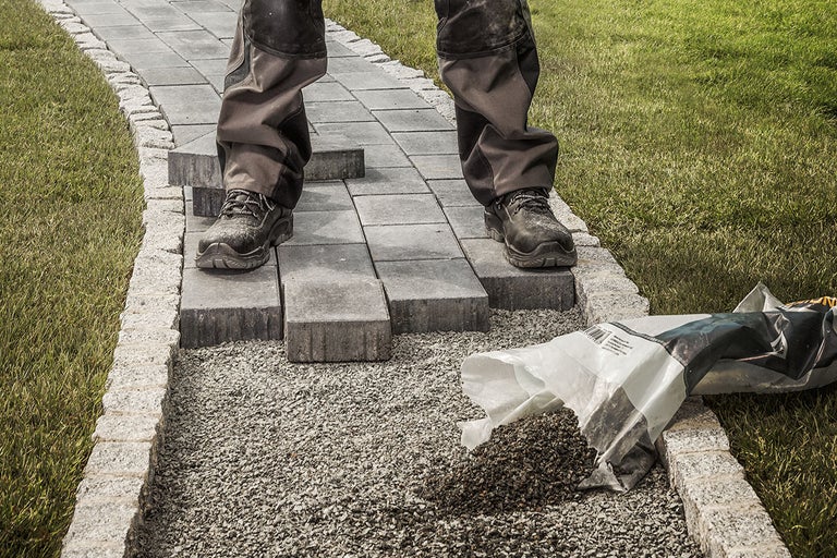 Stensättningsarbete i trädgården med gatstenar, grus och en person