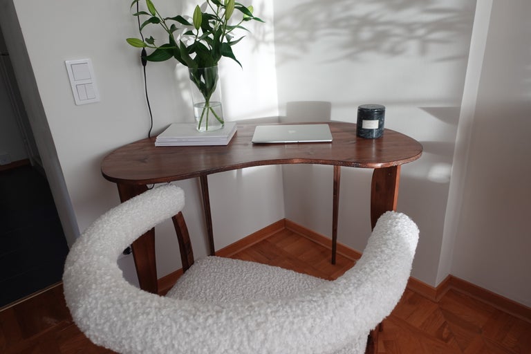 Skrivbord med laptop, ljus, anteckningsblock och blomvas, plus en stol med tygklädsel.