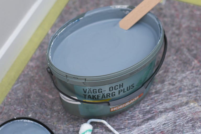 Hink med vägg- och takfärg samt en träpinne för omrörning.