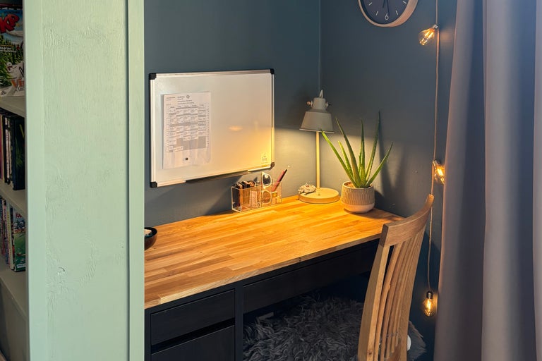 En organiserad arbetsplats med ett skrivbord i trä, skrivbordslampa, whiteboard och en Aloe Vera växt i en nisch.