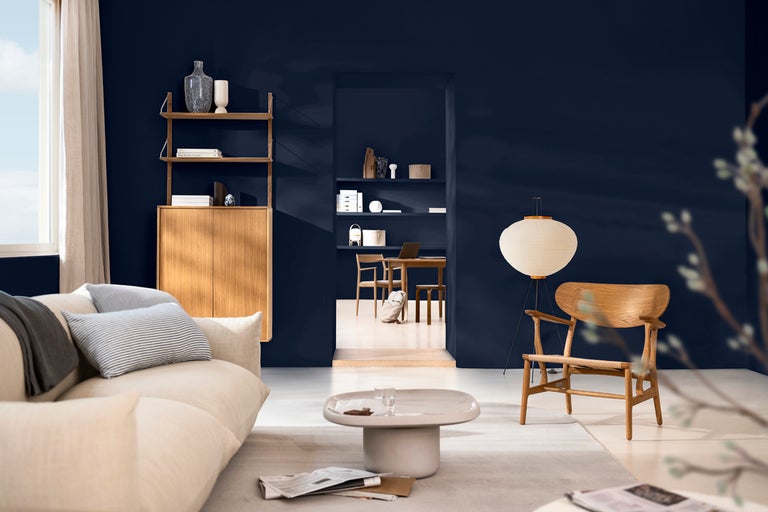 Vardagsrum med soffa, fåtölj, bord och hylla mot en mörkt målad vägg