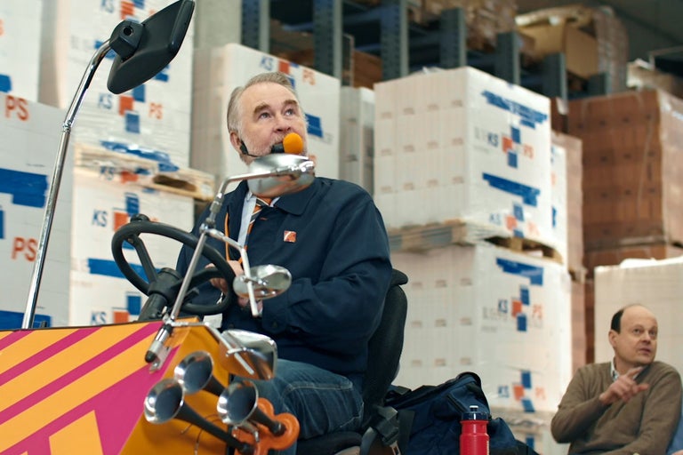 Man med headset och boll i munnen kör på ett dekorerat fordon genom ett lager