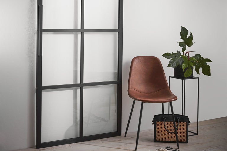 Rumsinteriör med svart skjutdörr med glasinsats, brun matrumsstol, växt på sidobord och handväska