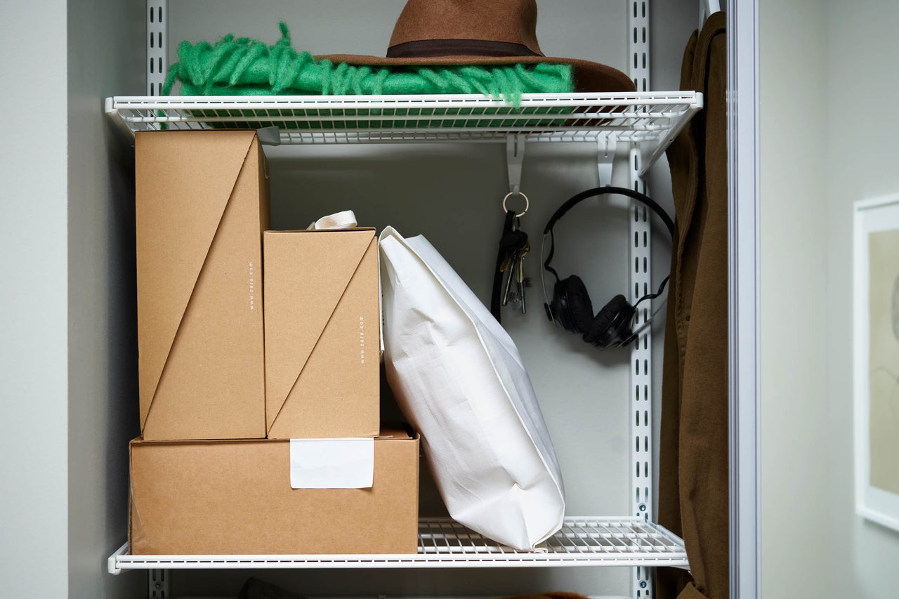 Organiserat skåp med hatt, ull, paket, väska, nycklar och hörlurar på vita metallhyllor
