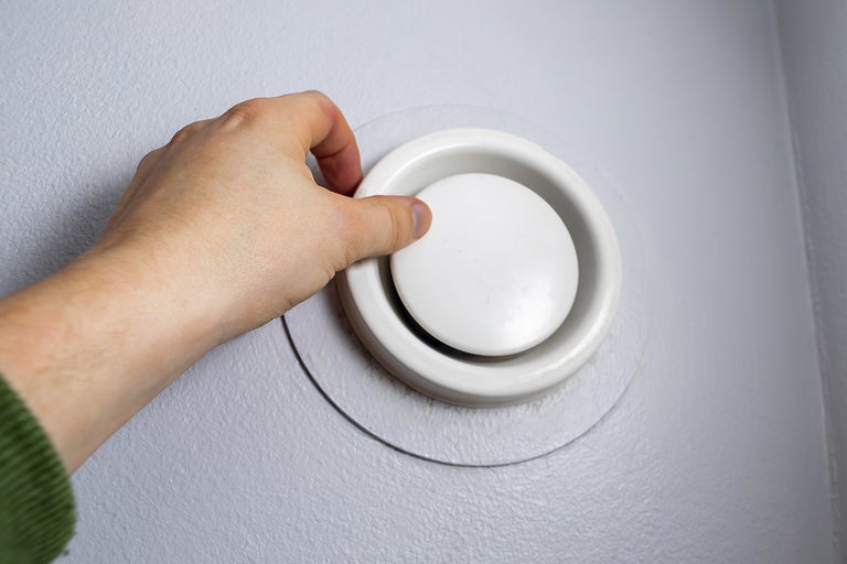 En hand justerar en rund tallriksventil på en vägg.