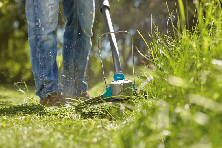En person använder en grästrimmer för att klippa gräs.