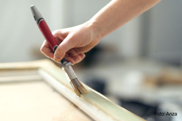 En person målar en träram med en pensel.