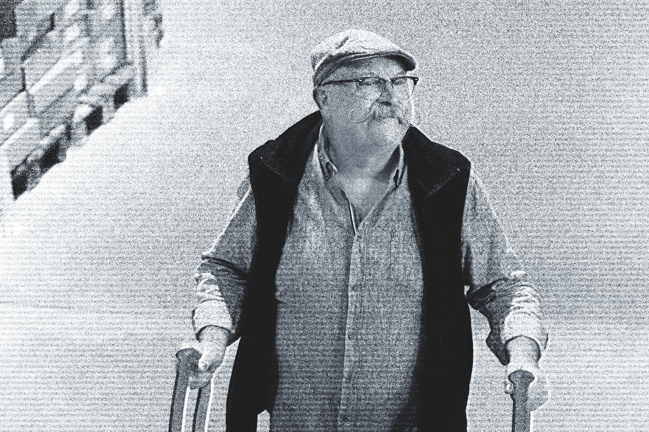 En man med hatt och skägg håller i en käpp.