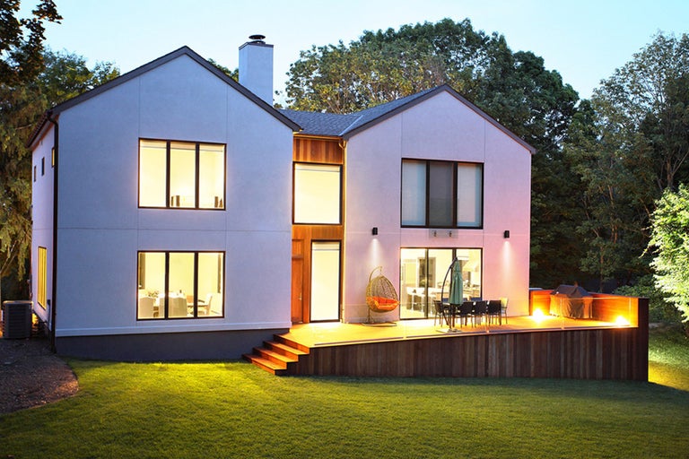 Modernt hus med träterrass och utemöbler utomhus.