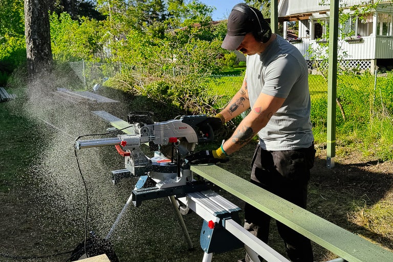 Hantverkare som sågar trä med en kap- och geringssåg utomhus.