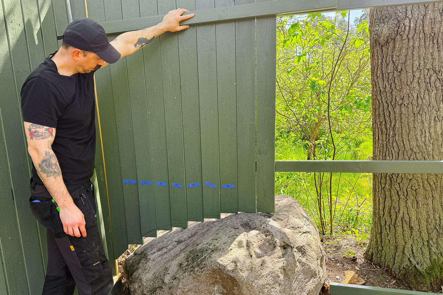 En man monterar ett staket på en solig dag i trädgården.