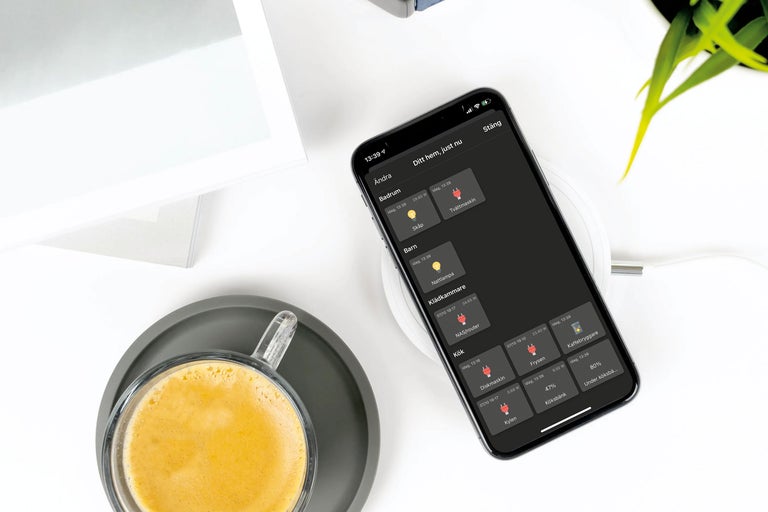 Smartphone med Smart Home-app på en trådlös laddare bredvid en kopp kaffe