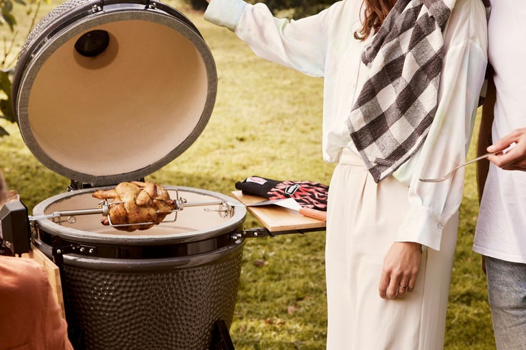 Scen med keramisk grill och stekt kyckling på spett i trädgården
