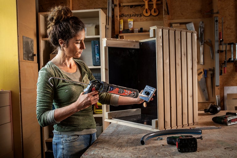 En kvinna applicerar monteringslim med en patronspruta på en del till en trälåda i en verkstad.