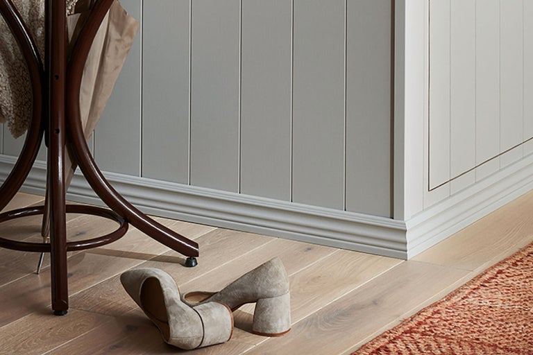 Scen med träpanel, golvsockel, klädhängare och skor på trägolv
