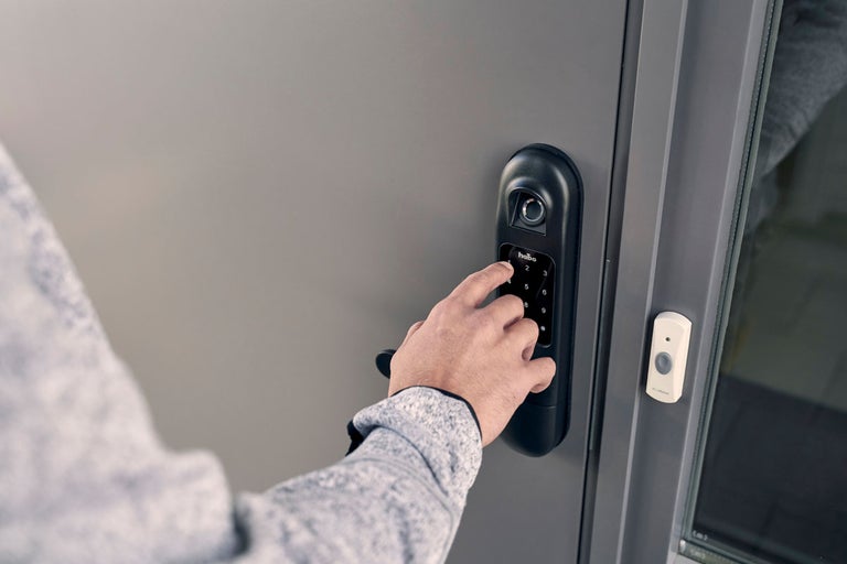 En person använder ett elektroniskt dörrlås med sifferkod och fingeravtryckssensor på en dörr.