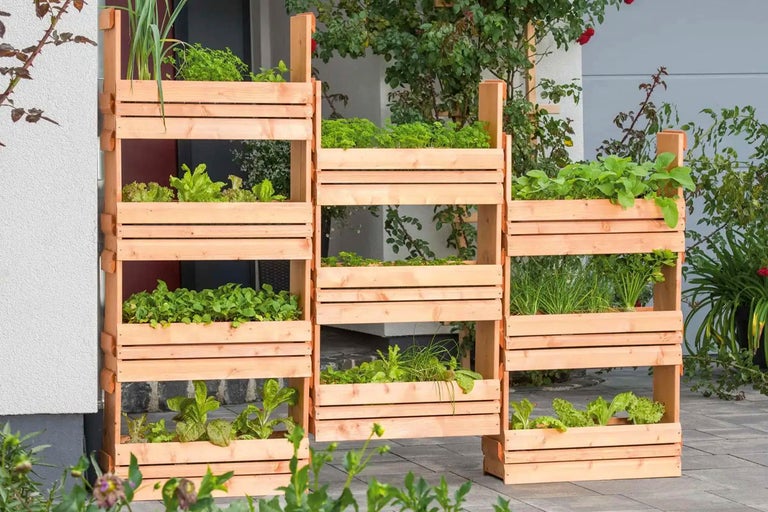 Tre planteringshyllor av trä med olika växter på en terrass