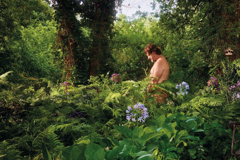 Lummig trädgård med ormbunkar, blommor och en person