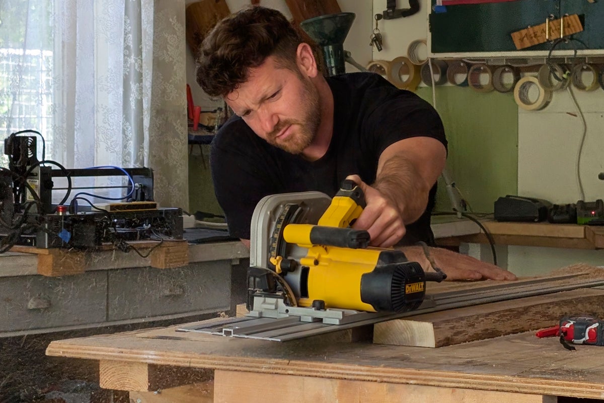 En hantverkare använder en DeWalt sänksåg med styrskena i en verkstad för att kapa en träplanka med precision.