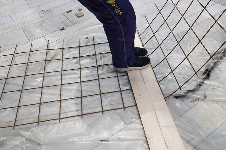 Person står på en träplanka över ett armeringsnät på plastfolie för att böja metallen.