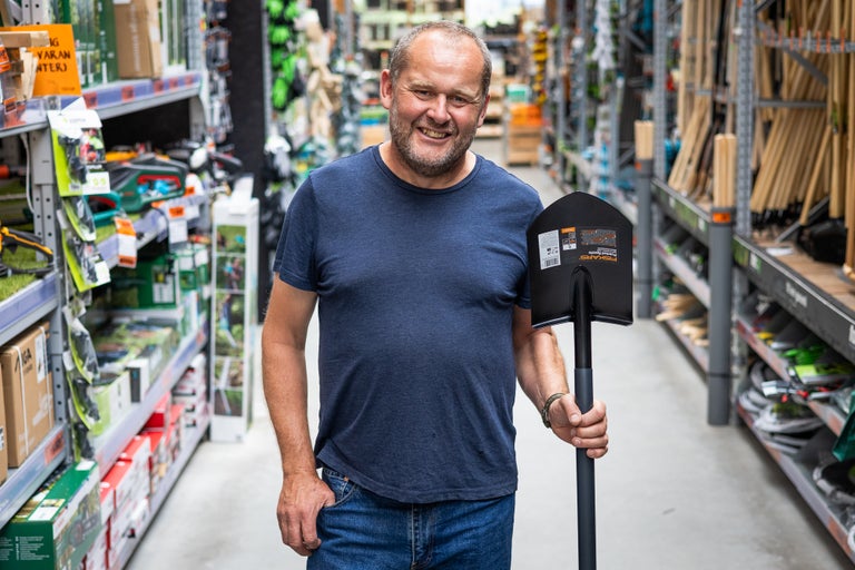 En man ler och håller en spade i ett Hornbach-varuhus.