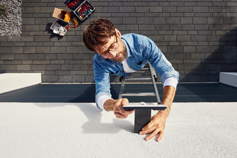 Man på en stege som fäster en takränna, med en verktygslåda i närheten.