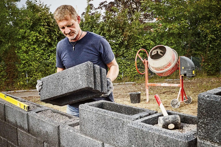 Man som lägger ljudisolerande stenar på en byggarbetsplats med betongblandare och gummiklubba
