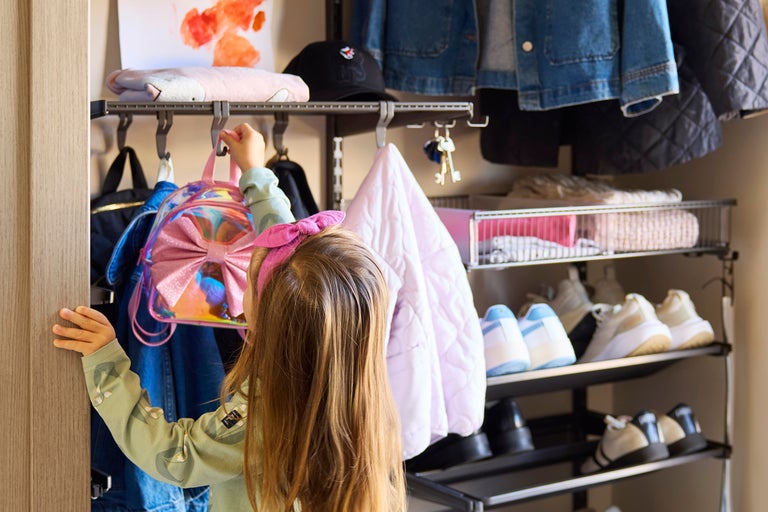 En flicka hänger en ryggsäck i en garderob med hyllor och klädstänger.