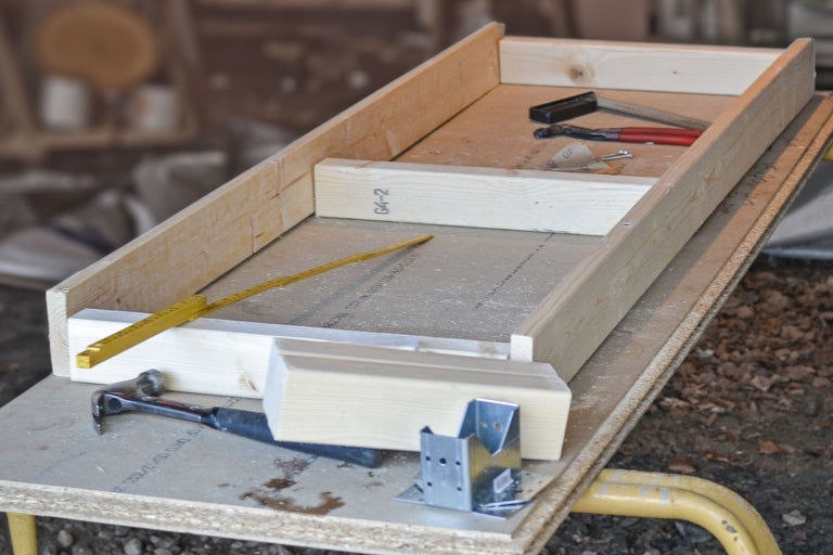 Träram med hammare, vinkelbeslag, tumstock och tång på en arbetsyta