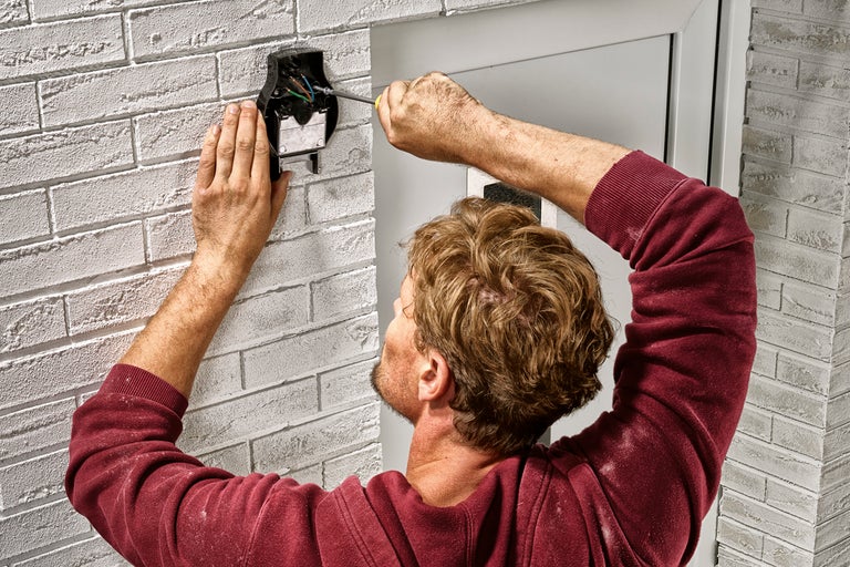 En man installerar en dörrklocka med en skruvmejsel på en vägg.