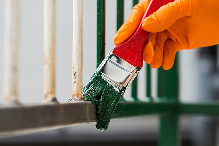 Hand med handske målar metallräcke med en pensel och grön färg