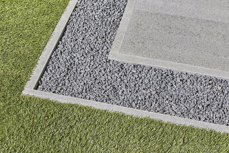 Närbild av en trädgård med gräsmatta, grus och en stenplatta.