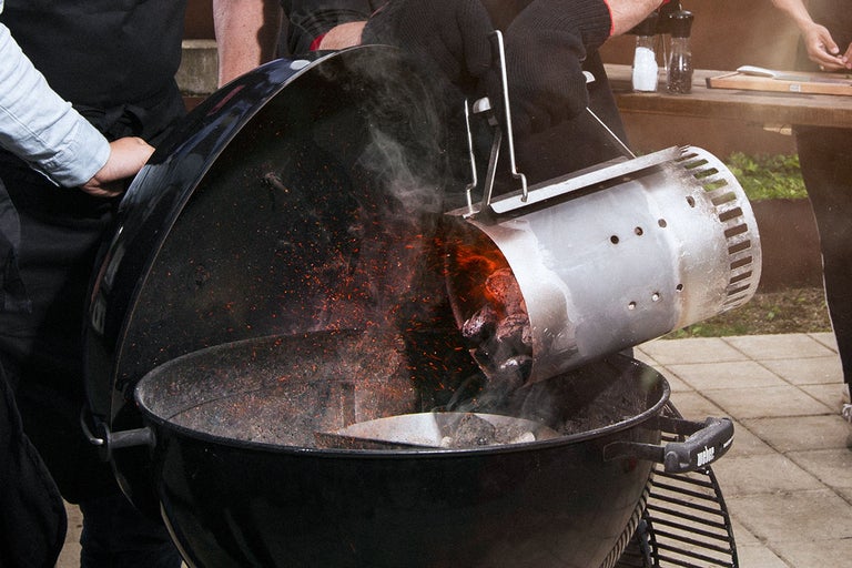 Person häller glödande kol från en tändrör i en grill.