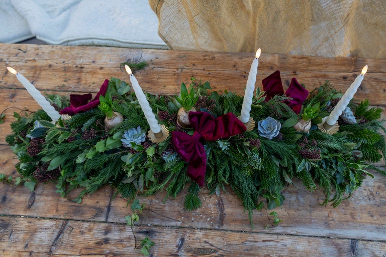 Juldekoration med ljus, grangrenar och rosetter på ett träbord