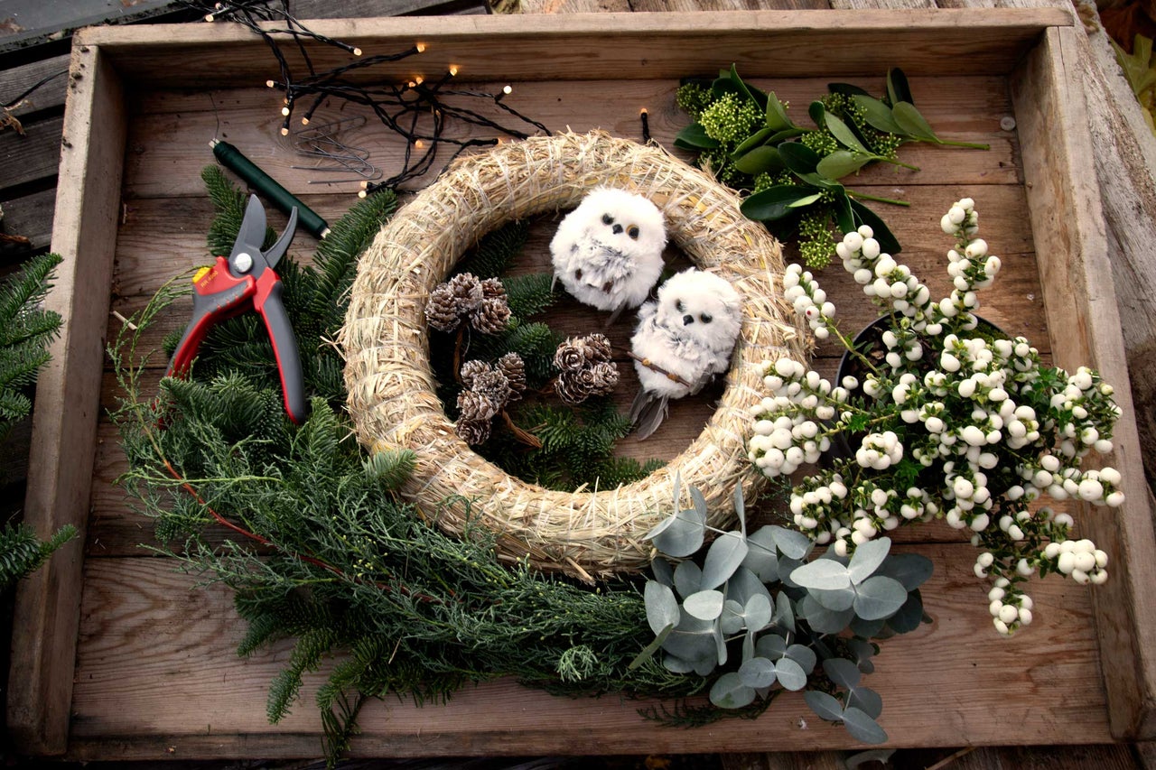 Trälåda med halmkrans, grangrenar, dekorationsugglor, barrträdskottar, grönska, bär, eukalyptus och trädgårdssax