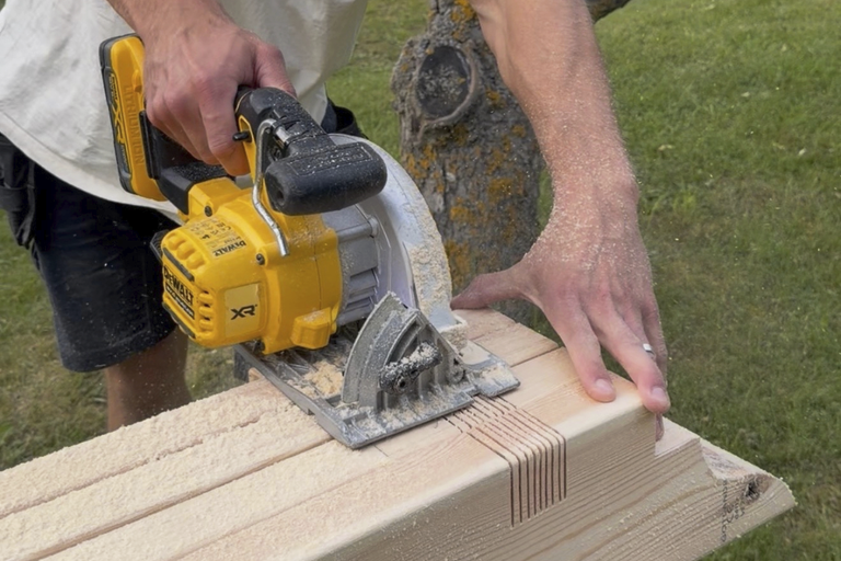 Person som sågar en träbalk med en batteridriven cirkelsåg från Dewalt utomhus.