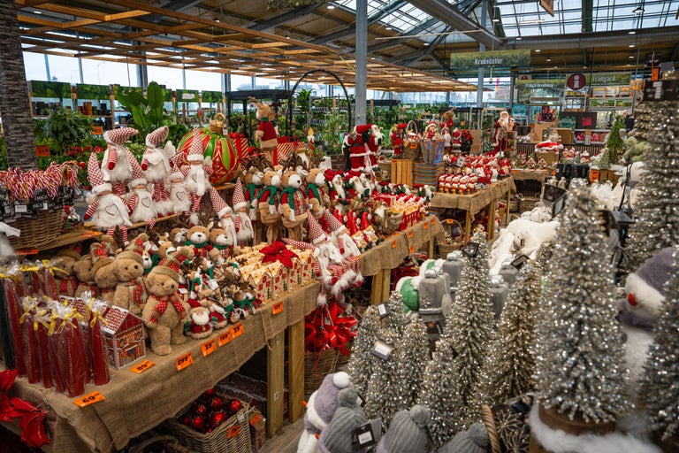 Dekorativ julavdelning med tygdockor, teddybjörnar, julgranar och juldekorationer i ett trädgårdscenter.