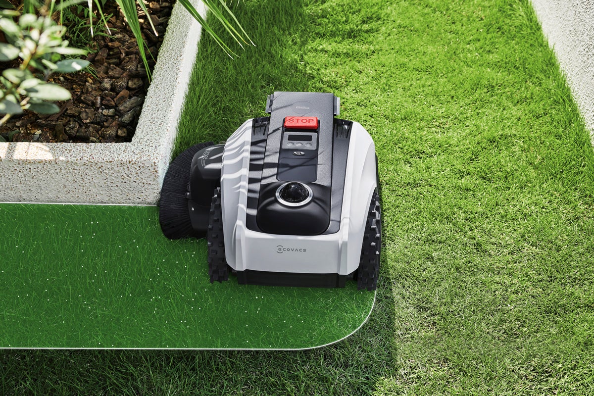 Ecovacs robotgräsklippare klipper precist längs en gräsmattekant i en ljus och välskött trädgård.