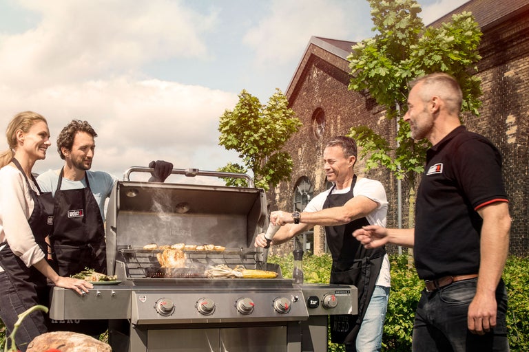 Grupp av människor grillar med en gasolgrill utomhus.