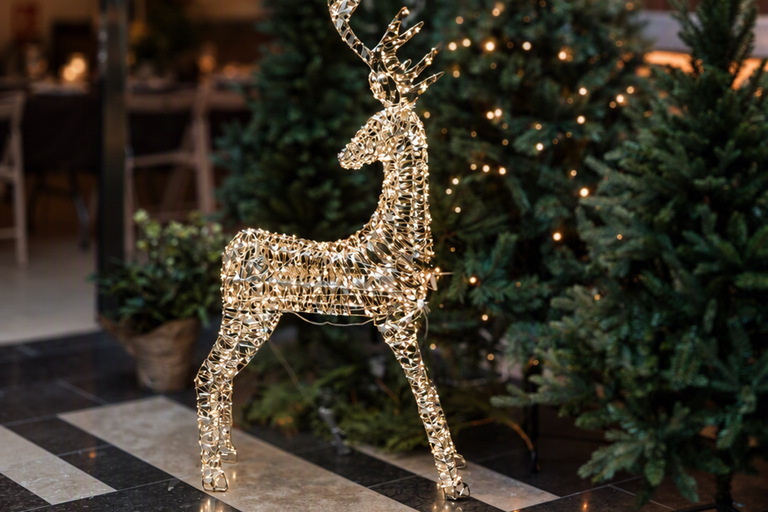 Belyst julfigur formad som en ren med LED ljusslinga framför två barrträd