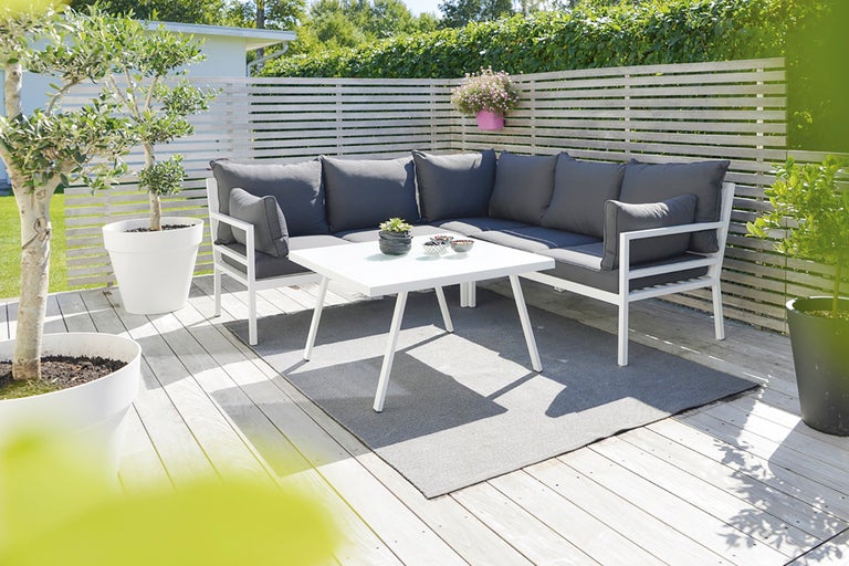 Trädgårdsscen med loungemöbler, bord och växter på en terrass.